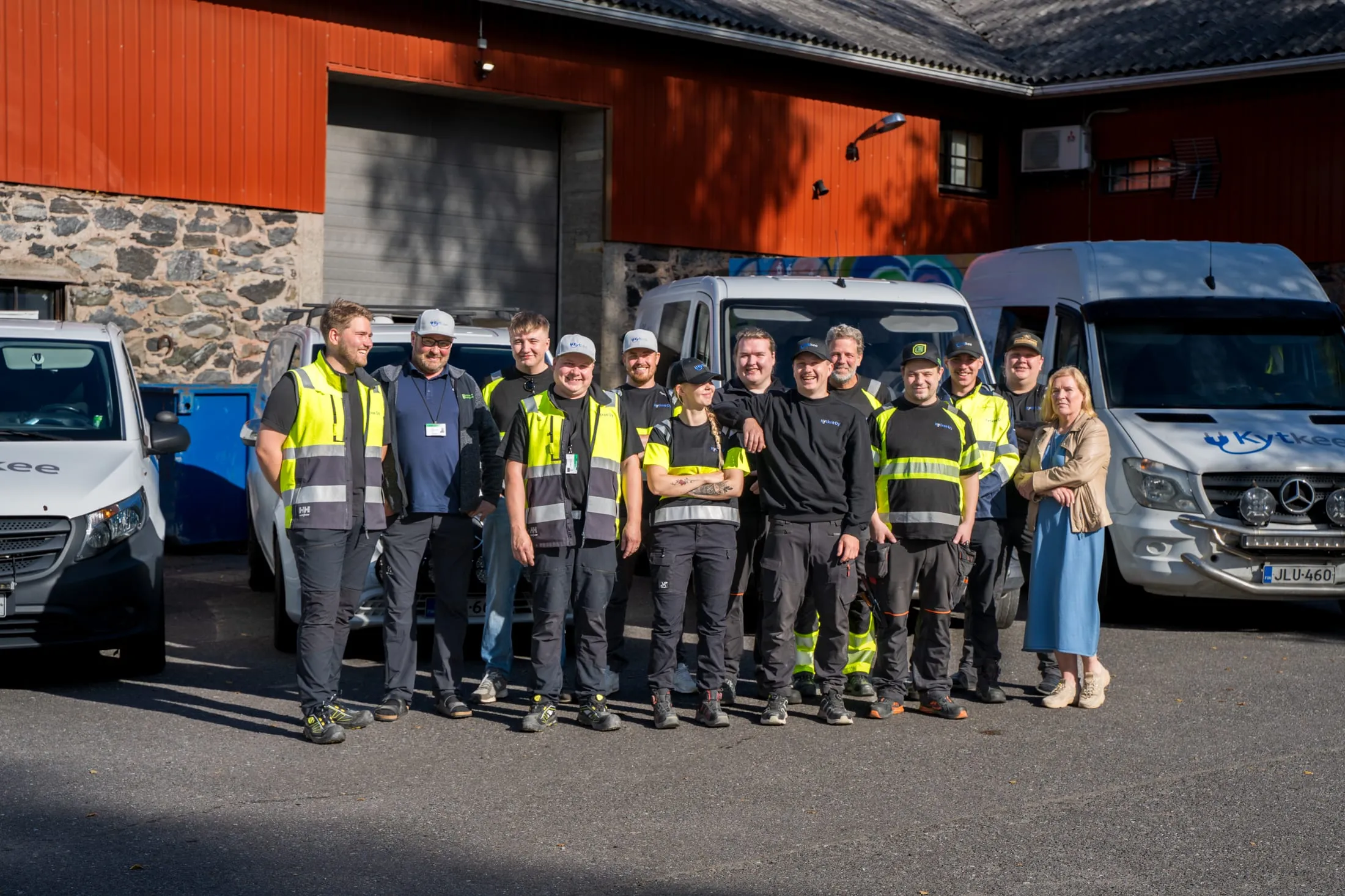 Kytkeen työntekijät ryhmäkuvassa yrityksen pihalla pakettiautojen edessä